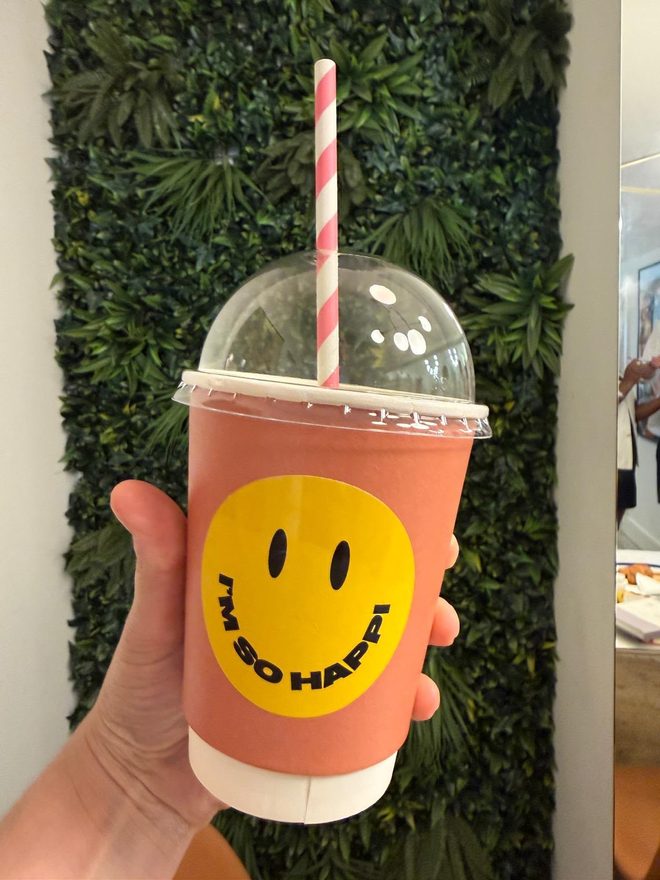 Pink iced smoothie held against a green foliage wall